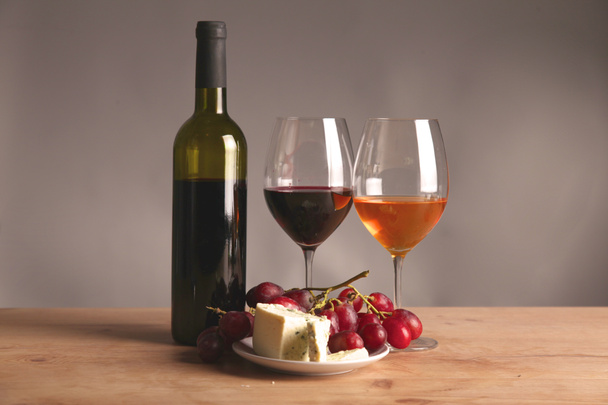 Verfijnde stillevens van wijn, kaas en druiven op rieten dienblad op houten tafel - Foto, afbeelding