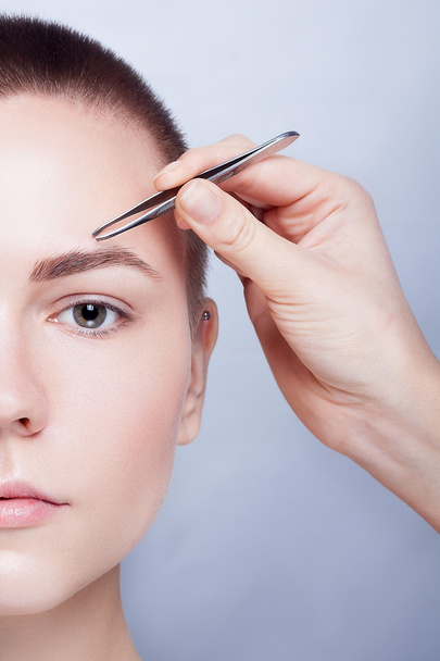 Young woman with short hair plucking eyebrows tweezers close up - Photo, image
