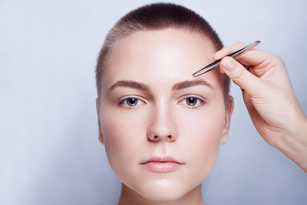 Young woman with short hair plucking eyebrows tweezers close up - Foto, Imagen