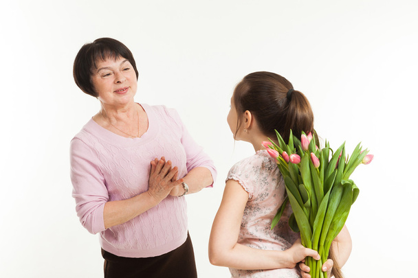 the granddaughter hides a bouquet of flowers for the grandmother - Foto, Imagen