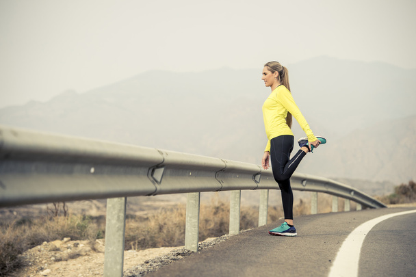 спортивная женщина растягивает мышцы ног после тренировки на асфальтированной дороге с сухим пустынным ландшафтом в жесткой тренировке
 - Фото, изображение