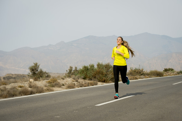若い魅力的なスポーツ女性砂漠山のアスファルトの道路上で実行 - 写真・画像