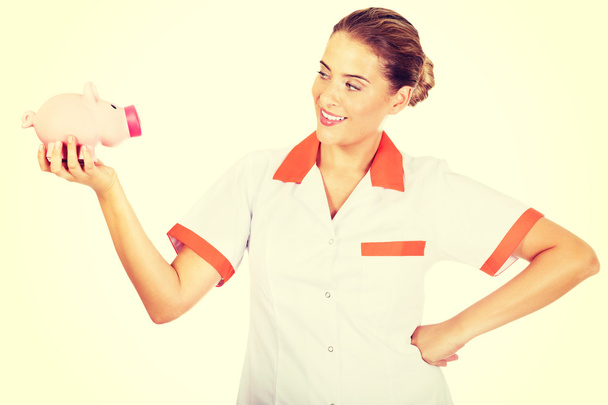 Young beautiful female doctor or nurse holding a piggybank - Фото, изображение