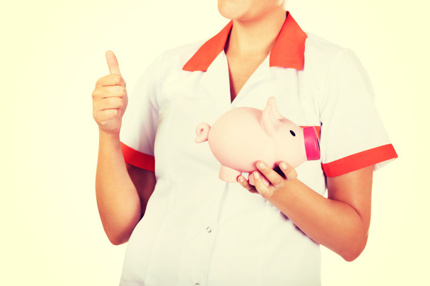 Young beautiful female doctor or nurse holding a piggybank - Фото, изображение
