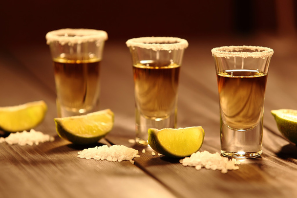 Three short glasses with alcohol next to a slice of lime and salt are on an old rustic table with vintage texture. Selective focus - Photo, Image