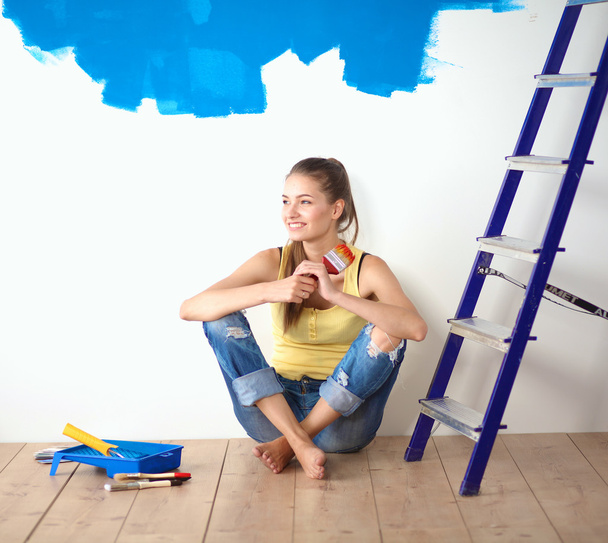πορτρέτο του ζωγράφου γυναίκα που κάθεται στο πάτωμα κοντά τοίχο μετά από την ζωγραφική. - Φωτογραφία, εικόνα