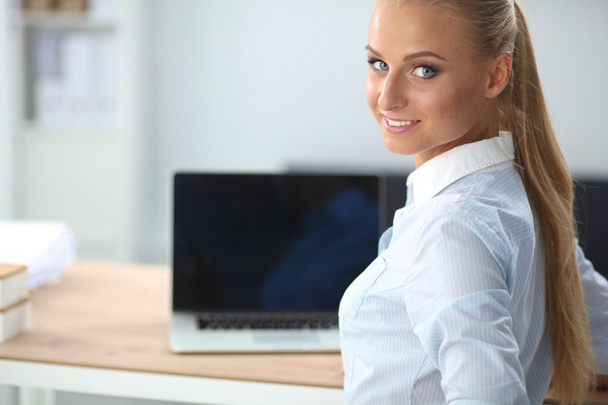 Attractive businesswoman sitting on a desk with laptop in the office - Zdjęcie, obraz