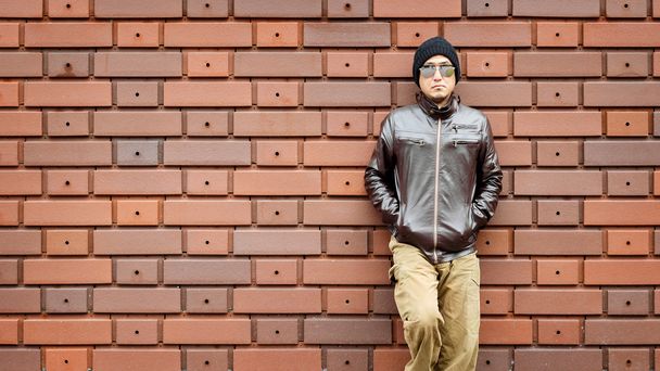 Um homem asiático em uma jaqueta marrom se inclina contra a parede
 - Foto, Imagem