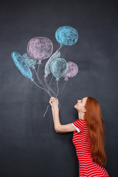 Cute woman holding colorful balloons drawn on chalkboard background - Foto, imagen