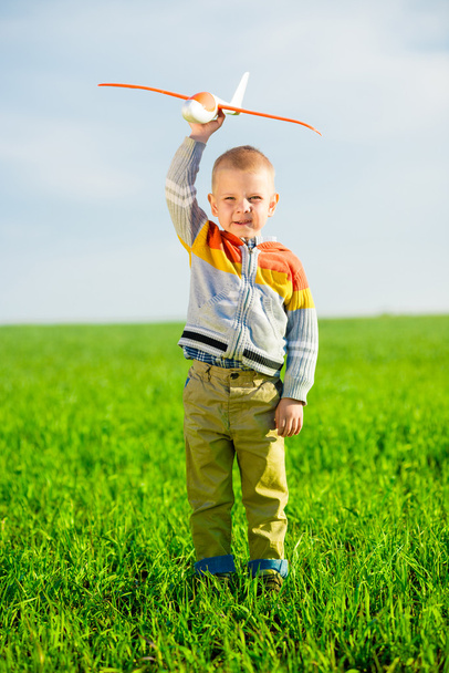 Felice ragazzo che gioca con aeroplano giocattolo contro cielo blu estate e sfondo campo verde
. - Foto, immagini