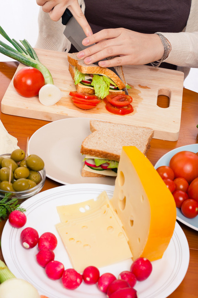 tabel met eten en vrouw halveren van sandwich - Foto, afbeelding