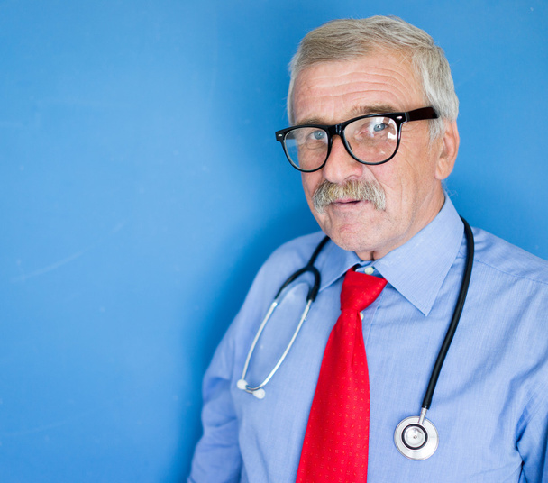 Portrait of a senior doctor on blue medical background - Photo, Image
