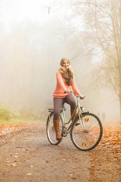 Happy active woman riding bike in autumn park. - Фото, изображение
