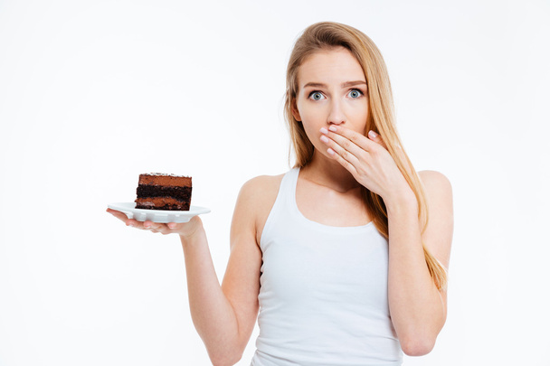 Beautiful confused woman on diet holding piece of chocolate cake - Zdjęcie, obraz