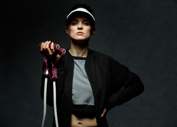 Young fit woman holding resistance band against dark background - Fotoğraf, Görsel