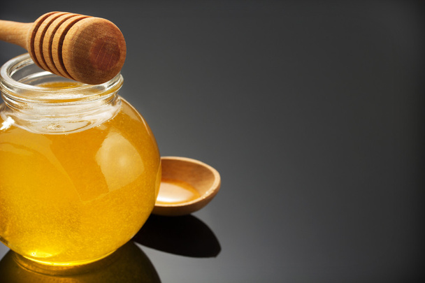 glass jar of honey and stick on black - Фото, изображение