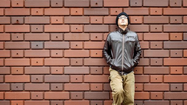Un asiatico uomo in una giacca marrone si appoggia contro il muro
 - Foto, immagini
