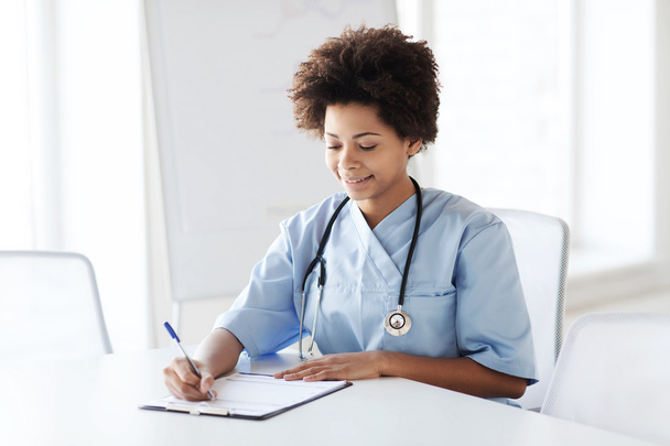 happy female doctor or nurse writing to clipboard - Photo, image