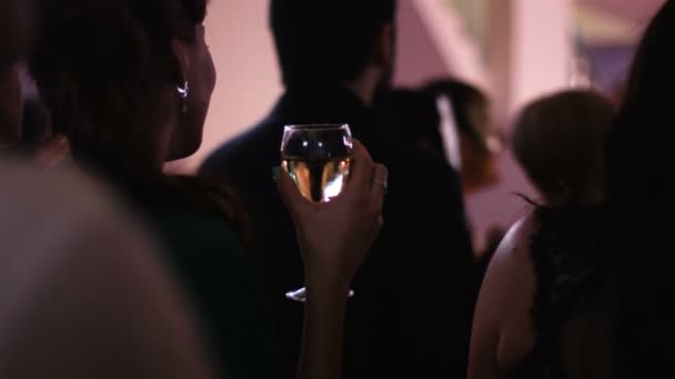 カメラに戻って若い魅力的な女性立っているとパーティーで白ワインのガラスを保つため、ステージ パフォーマンスが起こって見て. - 映像、動画