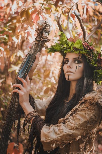 Portrait of a brunette with a painted face in the image of shaman and floral wreath on her head and horns - 写真・画像