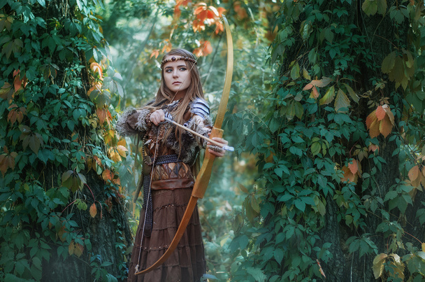 Mujer cazadora con un arco en la mano, apuntando a su presa en el bosque. Amazonas con un arco en las manos del bosque
. - Foto, Imagen