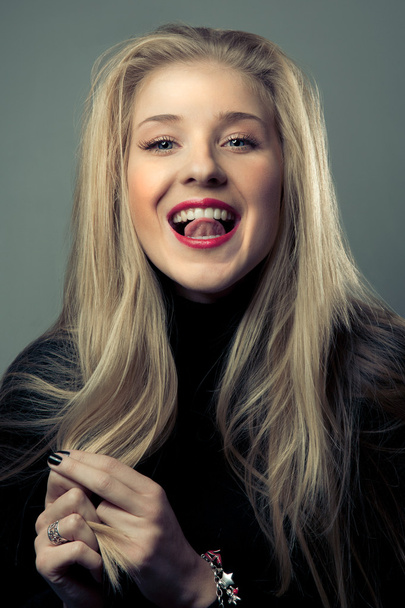 Portrait of emotional blond girl with hands near her face in black wear in studio with dark background - Foto, imagen