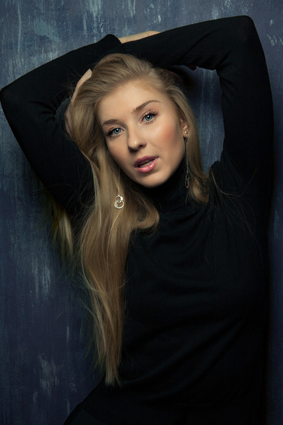 Portrait of emotional blond girl with hands near her face in black wear in studio with dark background - Foto, afbeelding