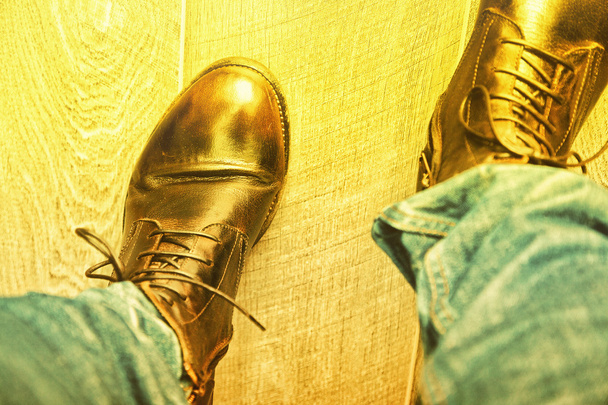 een man in trendy hoge laarzen en jeans gaat op de vloer. Kunst verlichting door zonlicht - Foto, afbeelding