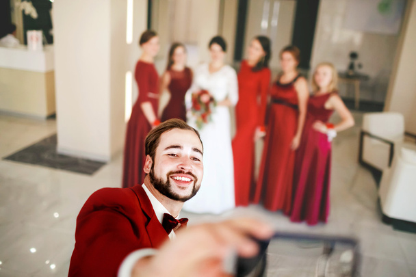 Groom makes selfie on background of bride with bridesmaids group photo. - Zdjęcie, obraz