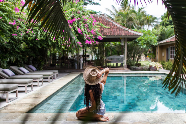 Молода струнка жінка розслабляється біля басейну з солом'яним капелюхом
 - Фото, зображення