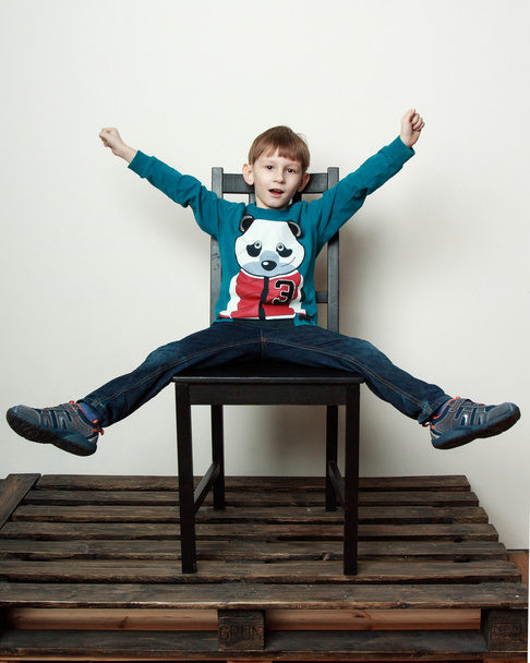  Маленький забавный мальчик сидит на стуле, прыгает, дурачится
 - Фото, изображение