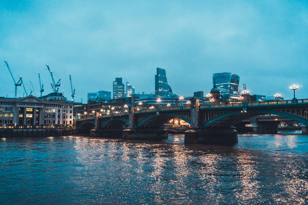 Most Southwark osvětlený pouličními světly a panorama města podél řeky Temže s výhledem na jeřáby na oblačný večer, Londýn, Anglie, Velká Británie - Fotografie, Obrázek