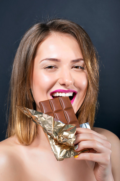 Bella nuda giovane donna bionda con trucco luminoso mangiare barretta di cioccolato
. - Foto, immagini