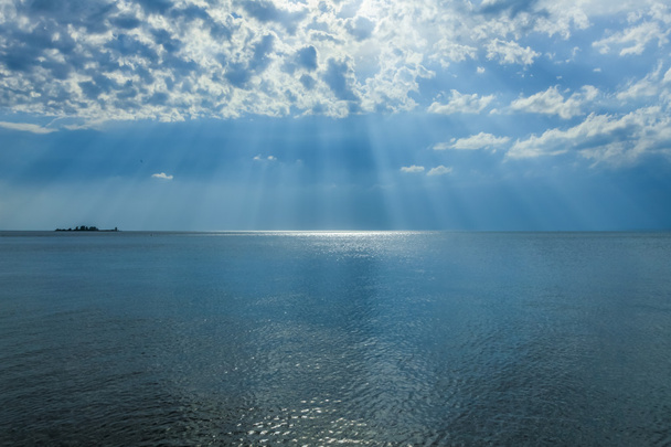 rayos de sol brillando a través de las nubes en el cielo azul sobre el mar
. - Foto, imagen