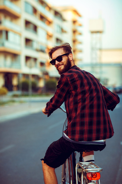 Young man in sunglasses riding a bike on city street - Photo, image