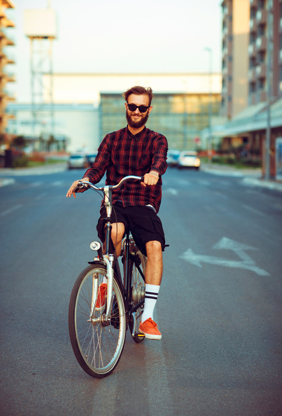 Young man in sunglasses riding a bike on city street - Фото, изображение