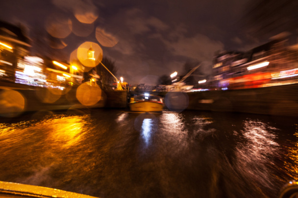 Отражения ночного освещения в Амстердамских каналах от движущегося круизного судна. Размытое абстрактное фото в качестве фона
. - Фото, изображение