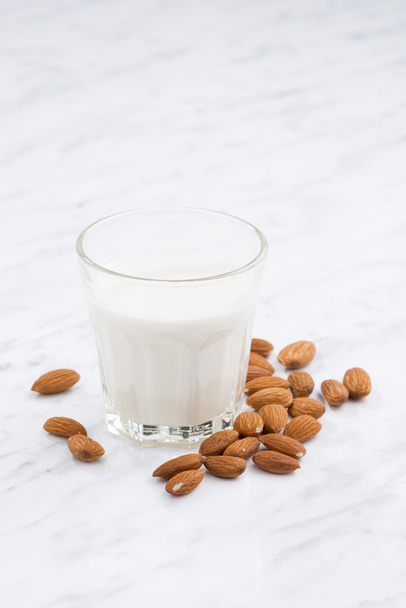 almond milk in a glass on white table, vertical - Фото, зображення