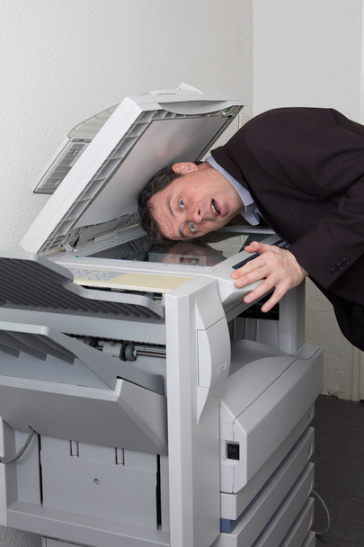 Vista lateral de un hombre poniendo su cabeza en una fotocopiadora
 - Foto, imagen
