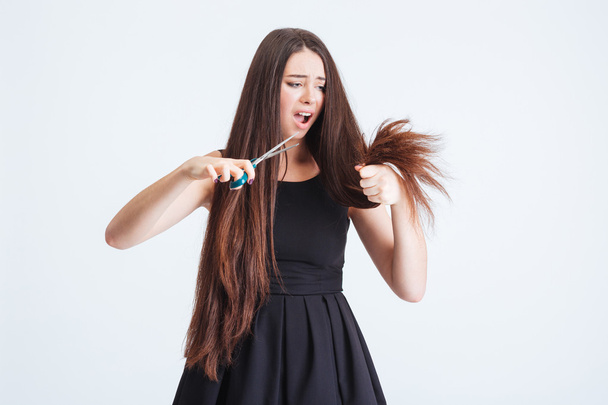 Shocked unhappy woman trimming split ends of hair with scissors  - Φωτογραφία, εικόνα