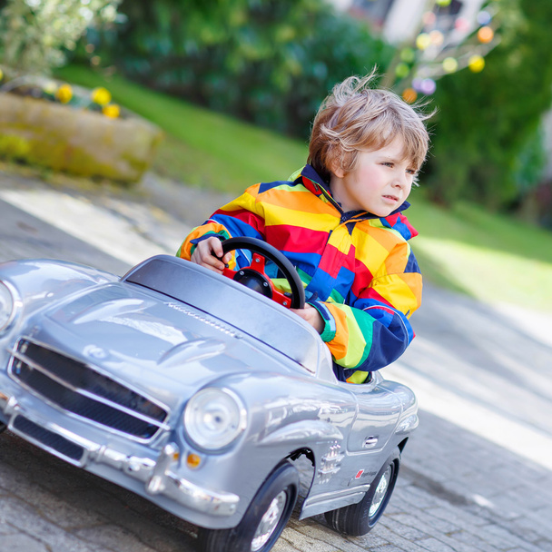 Маленький дошкольник за рулем большой игрушечной старинной машины, на открытом воздухе
 - Фото, изображение