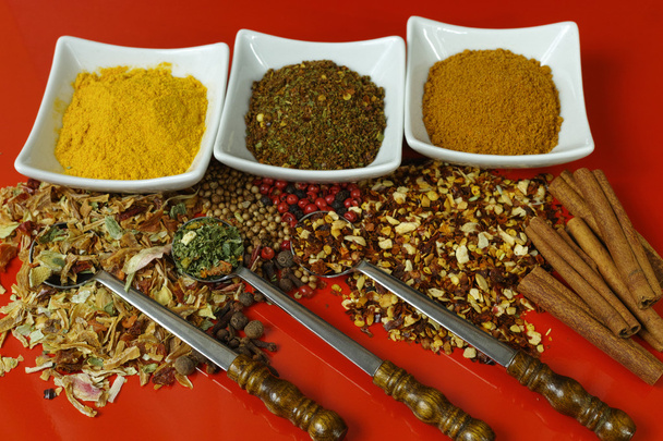 Joukko mausteita ja mausteita vanhalla metallilusikalla punaisella pöydällä
  - Valokuva, kuva