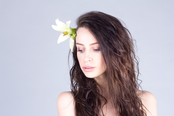 Woman with long curly hair and lily in hair looking down. SPA and beauty. - Foto, imagen