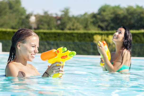 pretty girls playing with water guns in pool - 写真・画像