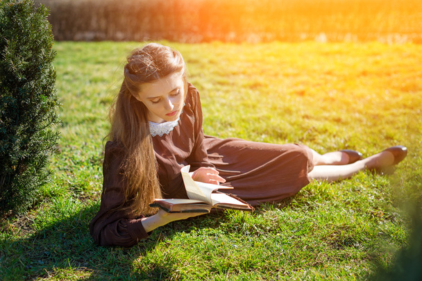 Romanttinen nuori nainen lukee kirjaa puutarhassa istuu nurmikolla. Rentoudu ulkona aika käsite. - Valokuva, kuva