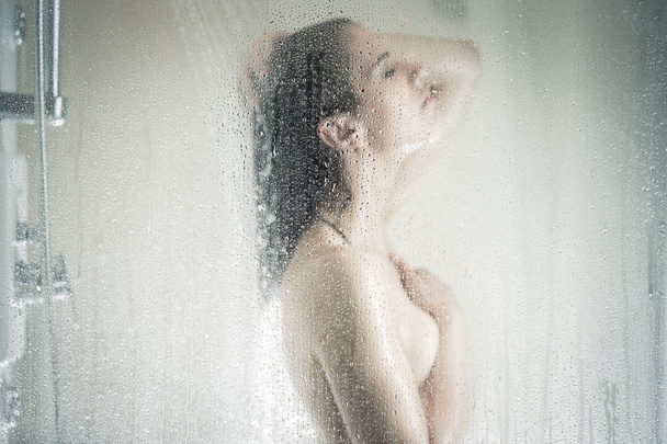 Relief and relaxation after long stressful day.Taking moment for yourself concept.Skincare,spa and aromatherapy.Unfocused portrait of a woman showering through the bath screen with little drops - Foto, Imagem
