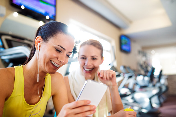Two attractive fit women in gym with smart phone - Fotoğraf, Görsel