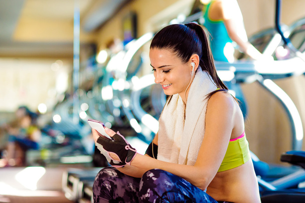 Femme en forme attrayant dans une salle de gym avec téléphone intelligent - Photo, image