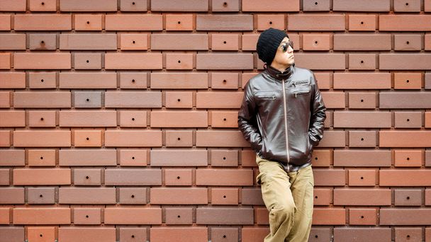 Um homem asiático em uma jaqueta marrom se inclina contra a parede
 - Foto, Imagem