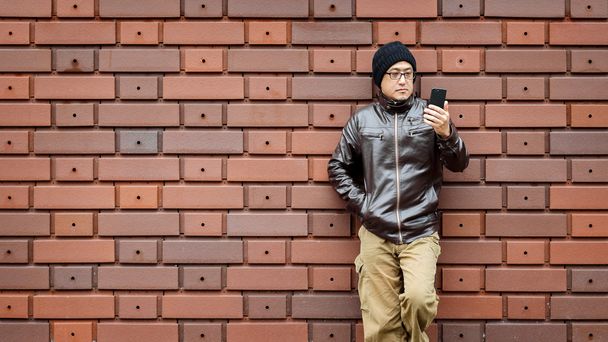 Un hombre asiático en una chaqueta marrón con su Smartphone
 - Foto, imagen